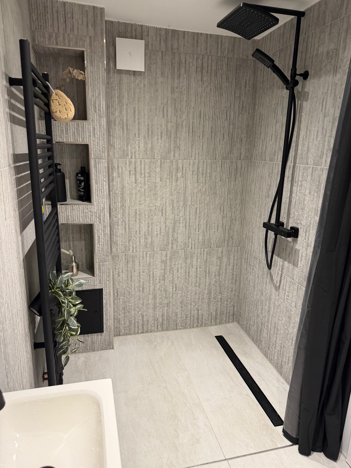 Bodengleiche Dusche mit strukturierten grauen Wandfliesen und schwarzen Armaturen