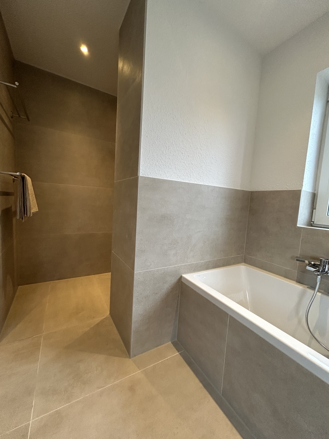 Badezimmer mit Wanne und offenem Duschbereich in warmer Steinoptik