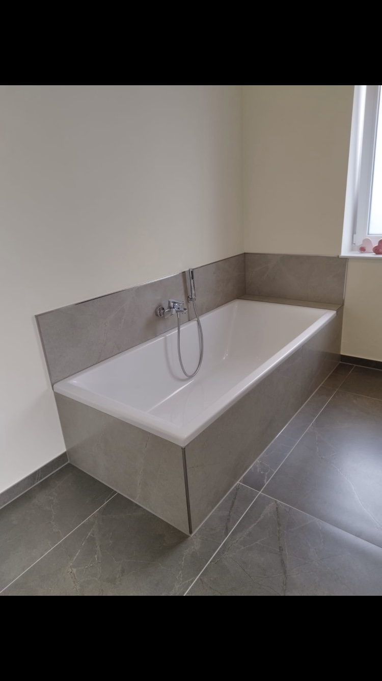 Badezimmer mit eingefliester Badewanne und grauen Natursteinoptik-Fliesen