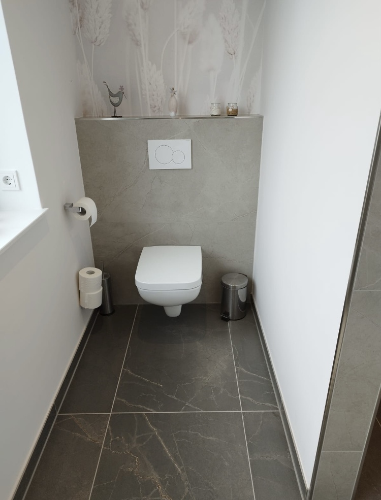 Modernes WC mit grauem Fliesenboden und gefliester Vorwand