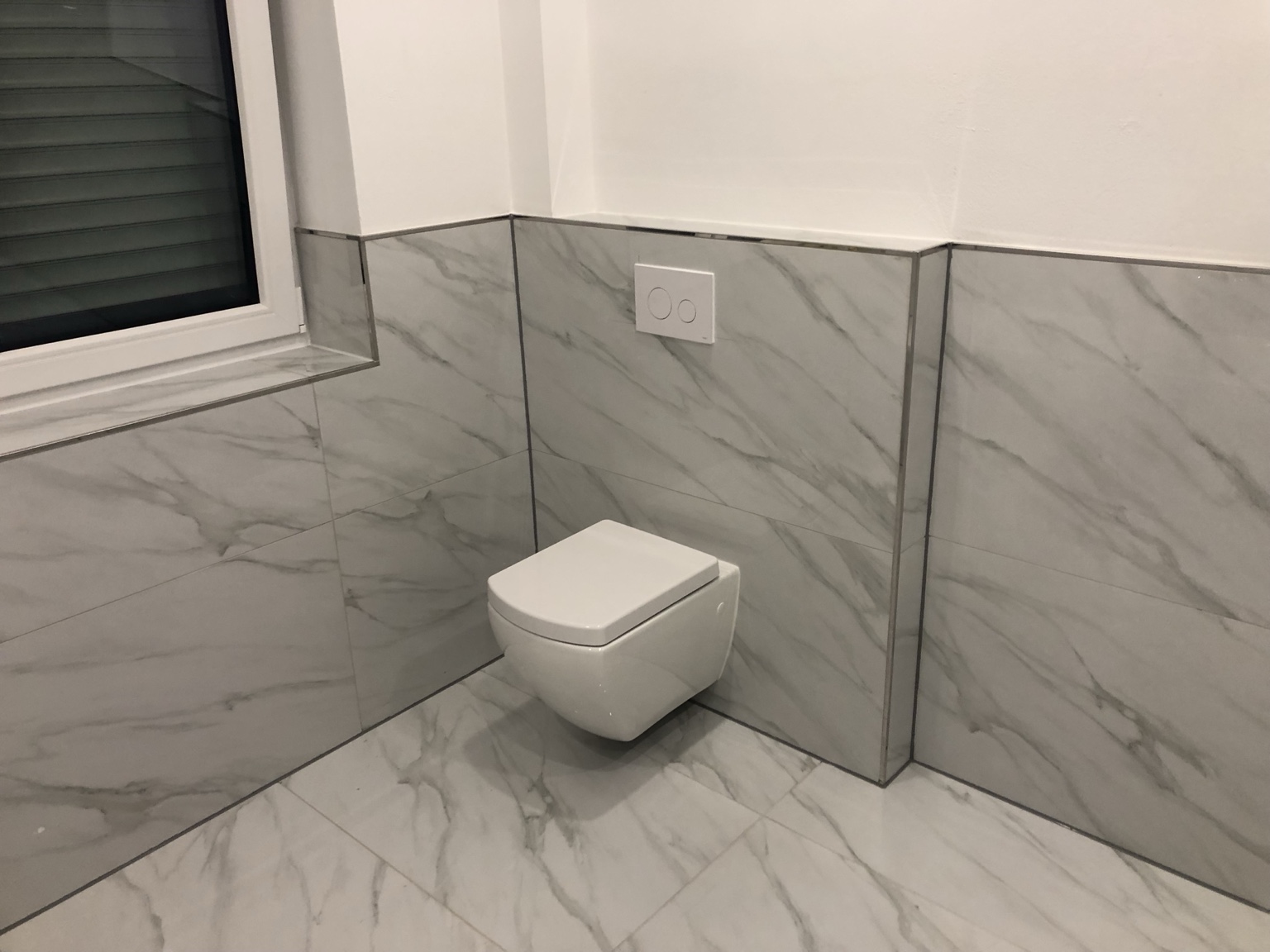 Badezimmer mit großformatigen Marmoroptik-Fliesen und Wand-WC