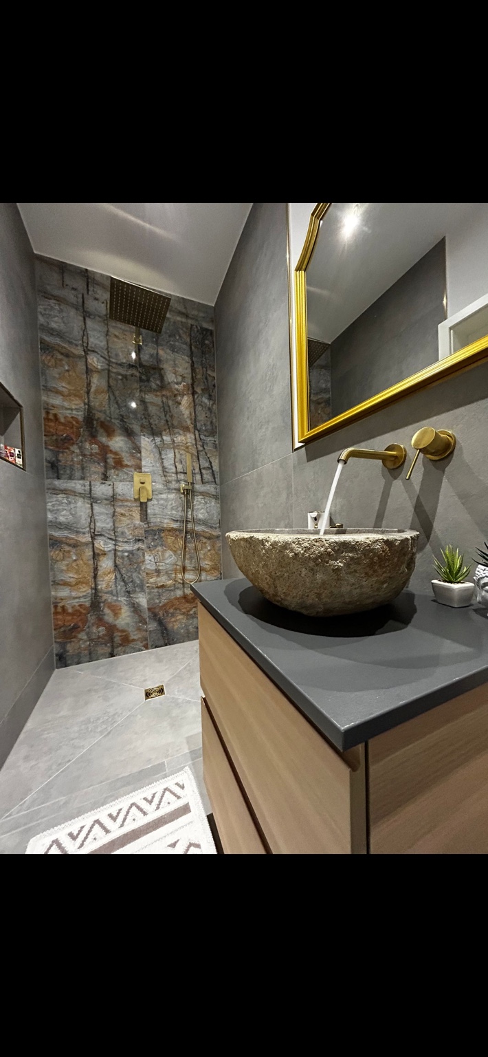 Exklusives Bad mit Natursteinwaschbecken, goldenen Armaturen und Akzentwand