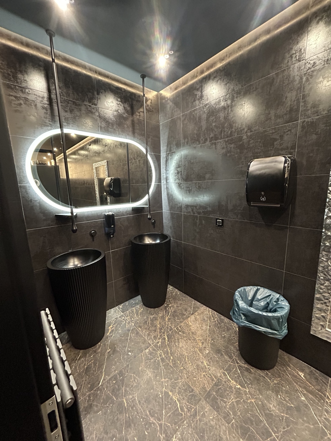 Modernes gewerbliches WC mit dunklen Wandfliesen und Marmoroptik-Boden
