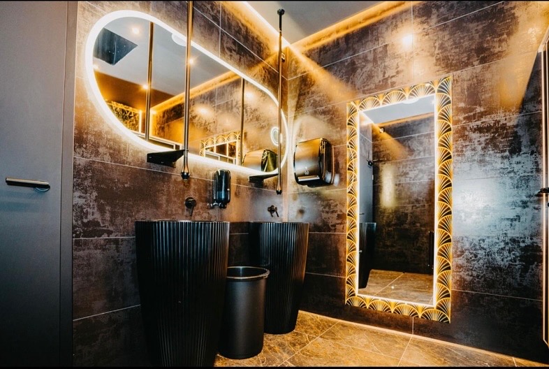 Gewerblicher Waschraum mit schwarzen Waschtischen und indirekter Beleuchtung