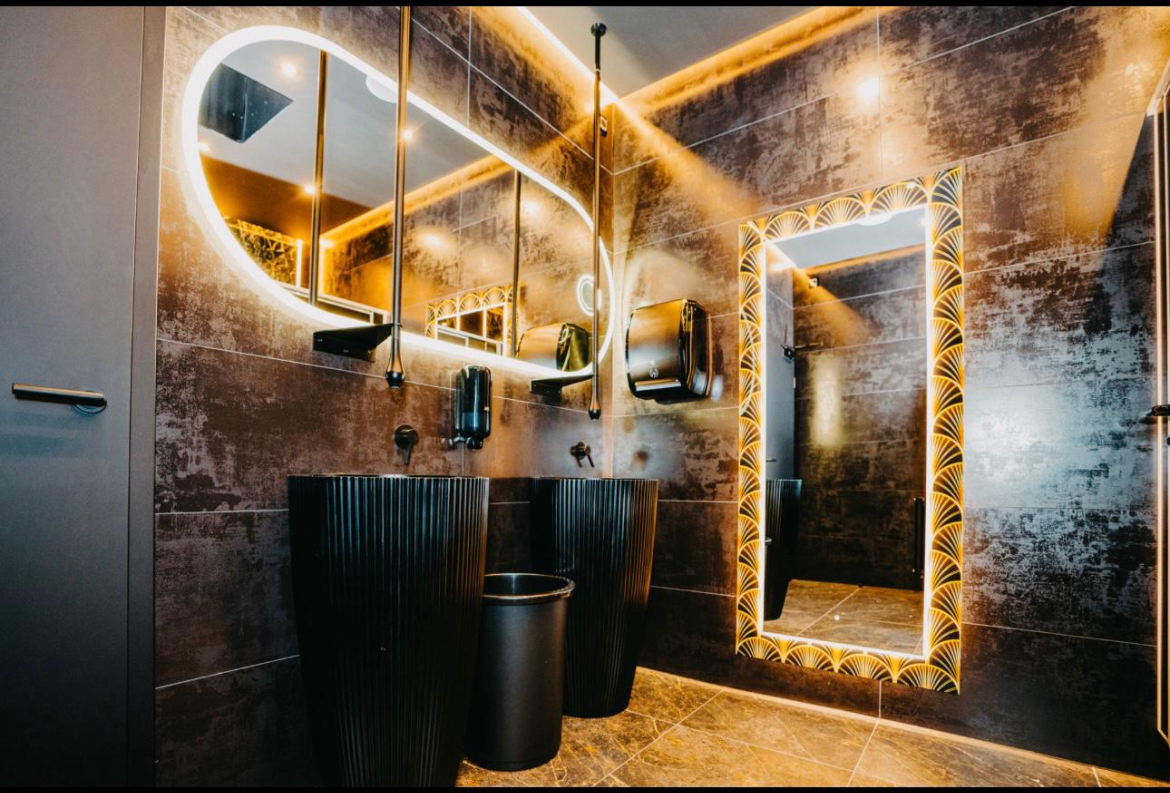 Exklusiver gewerblicher Waschraum mit beleuchteten Spiegeln und dunklen Fliesen