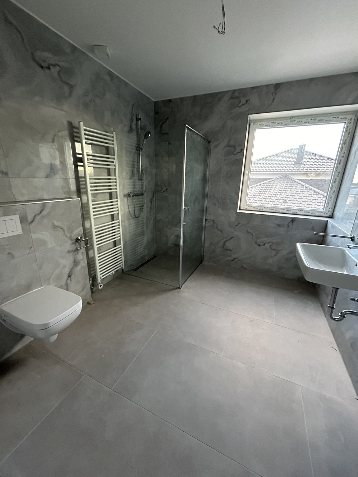 Großzügiges Bad mit marmorierten Wandfliesen und bodengleicher Dusche