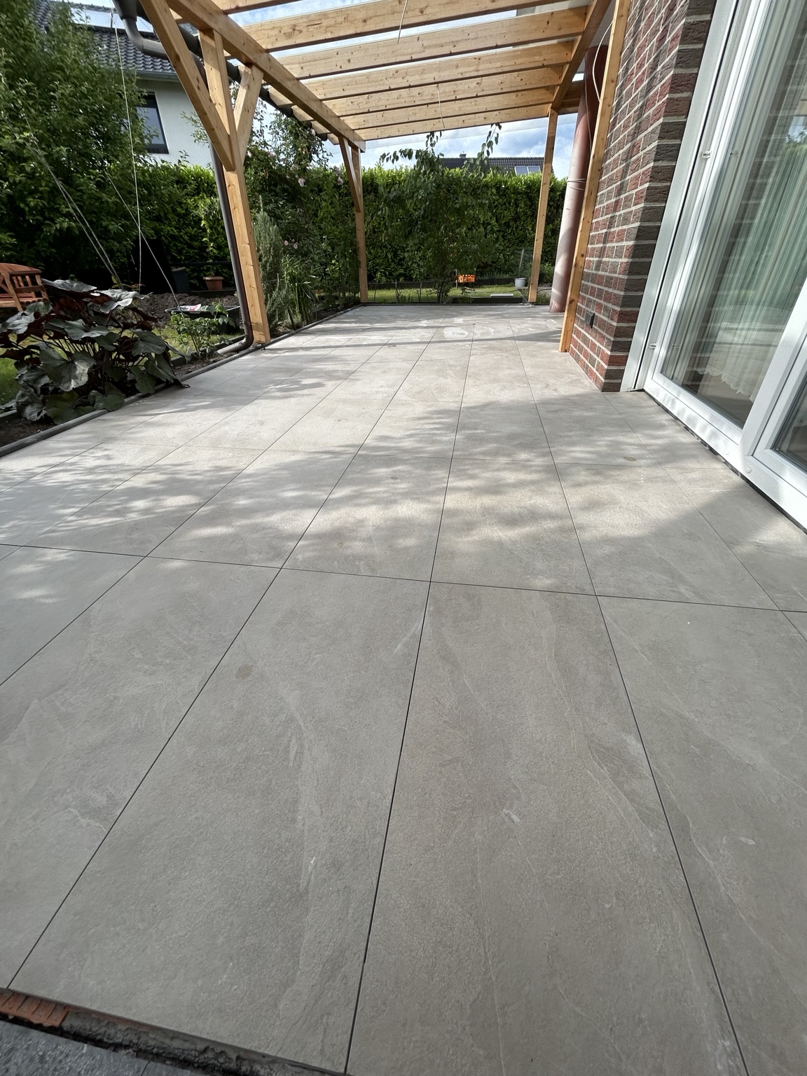 Großzügige überdachte Terrasse mit hellgrauen Bodenfliesen